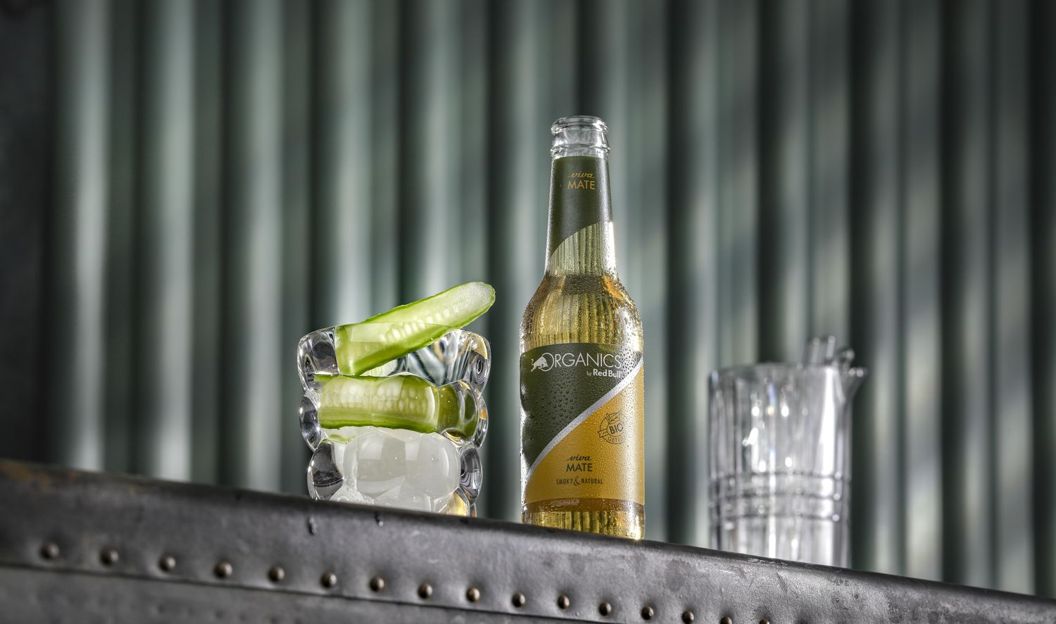 Fill a highball glass with ice cubes and place a long slice of cucumber in it